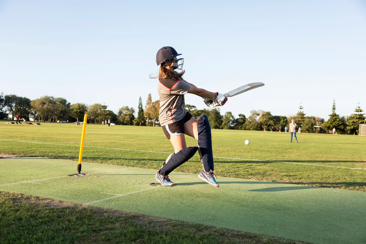 A female crickets bats on a sports field in the evening light