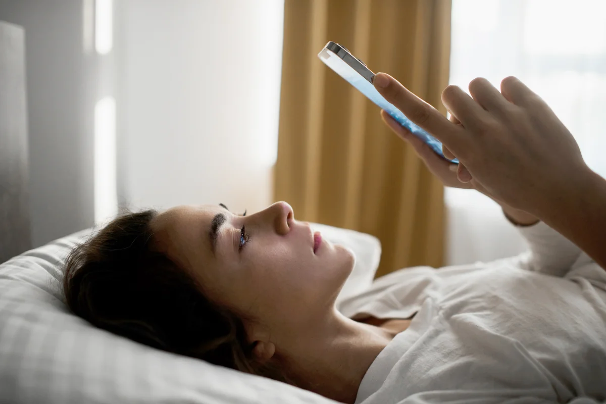 Sad and tired woman lying in bed with phone