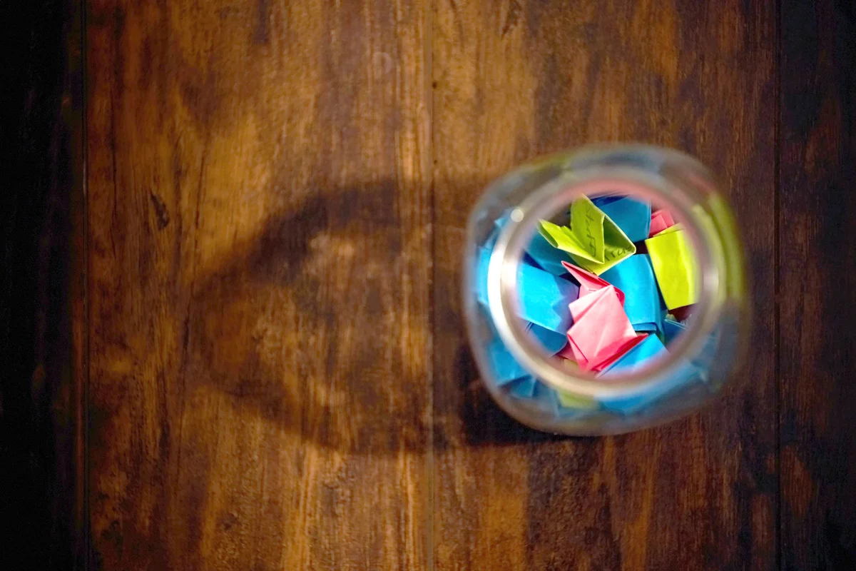 Little pieces of folded neon paper with some writing on them piled into a large mason jar