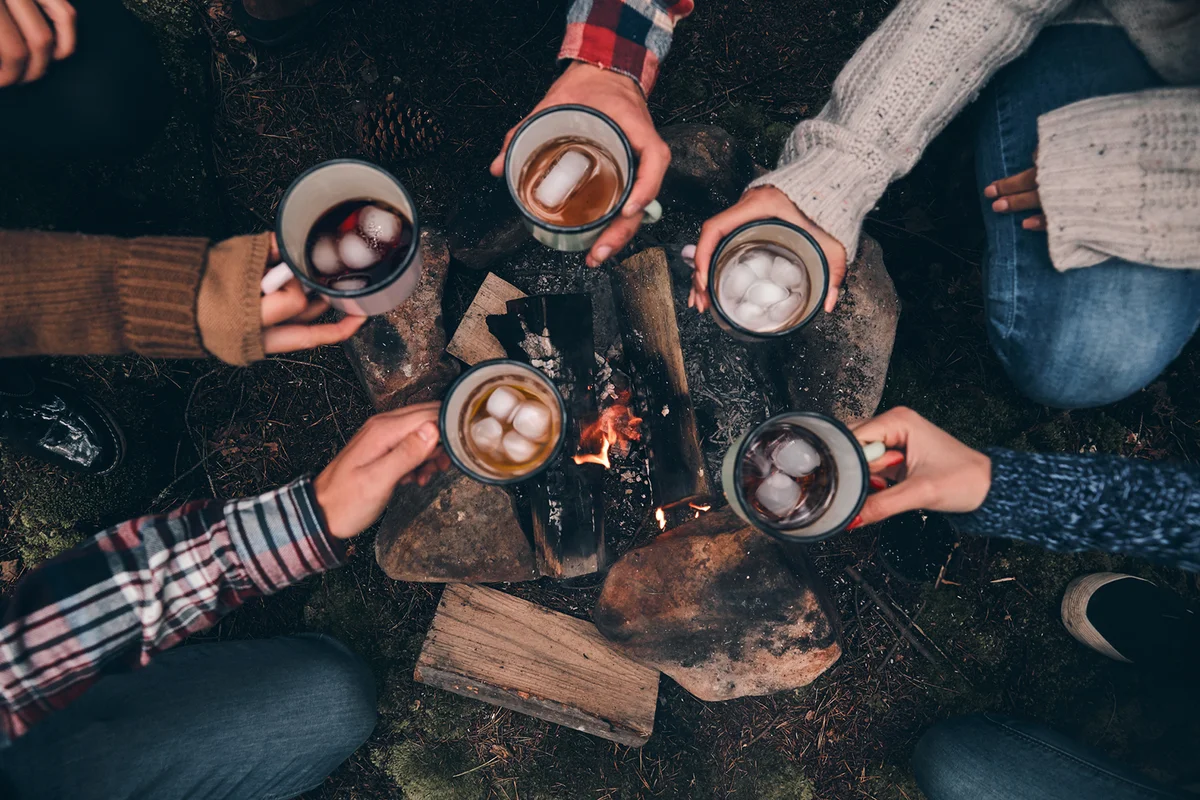 top view of young people toasting each other while warming up near the campfire in the woods