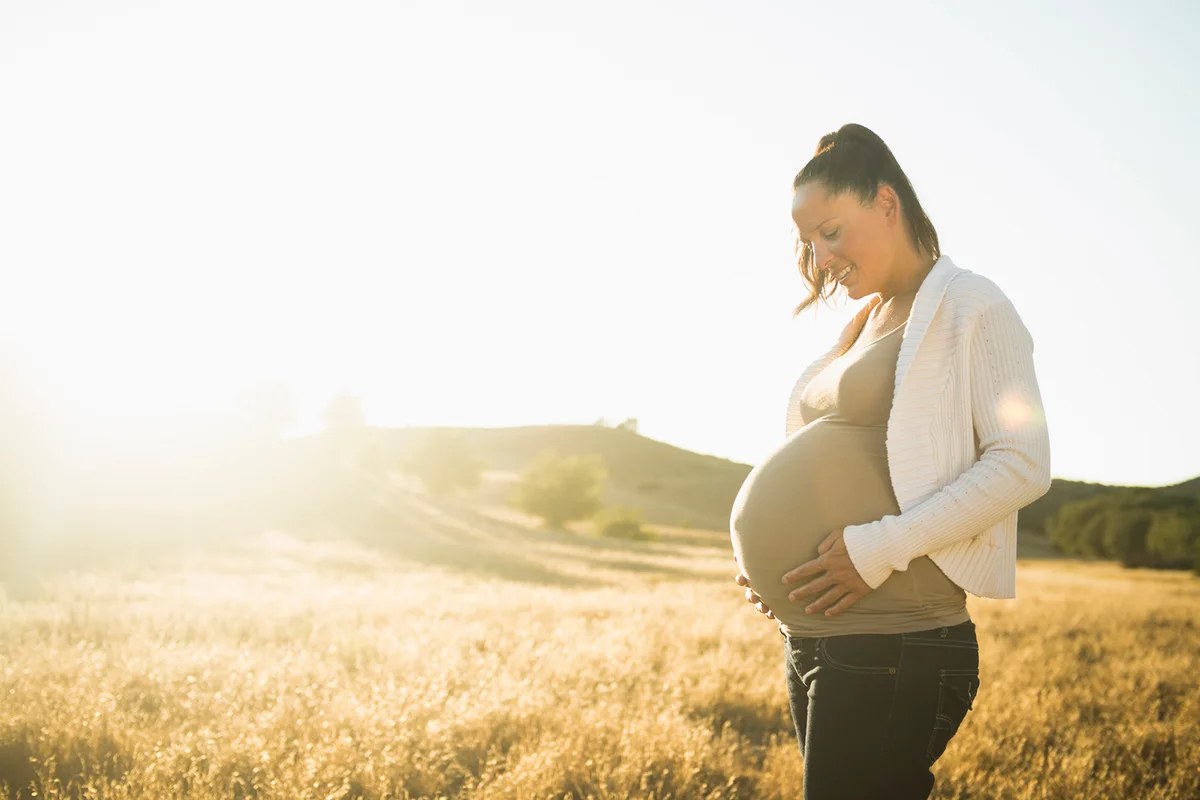 Pregnant woman holding stomach in rural field