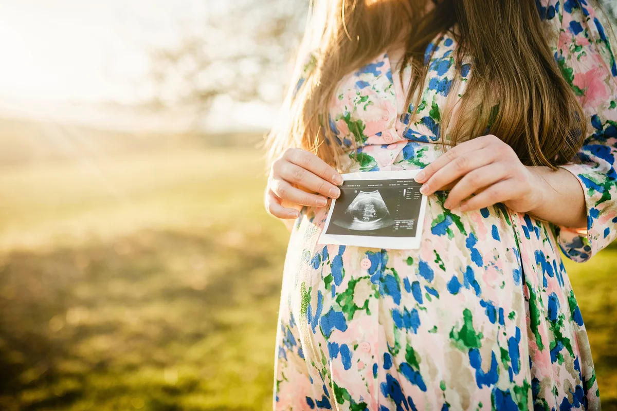 Unrecognizable pregnant woman in the nature with a photo of the baby