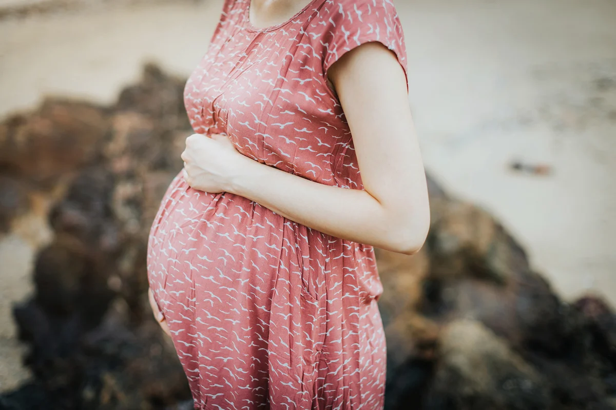 pregnant woman wearing a pink dress and holding her belly