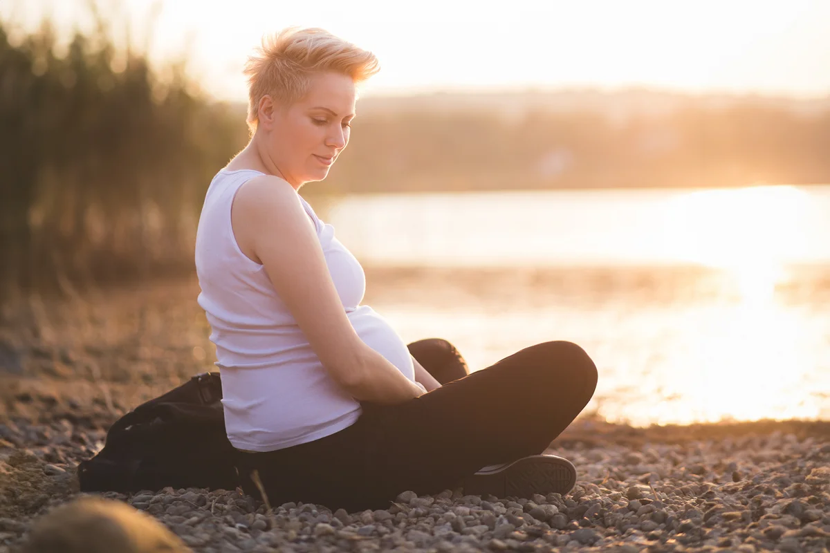 Pregnant woman touching her belly at sunset