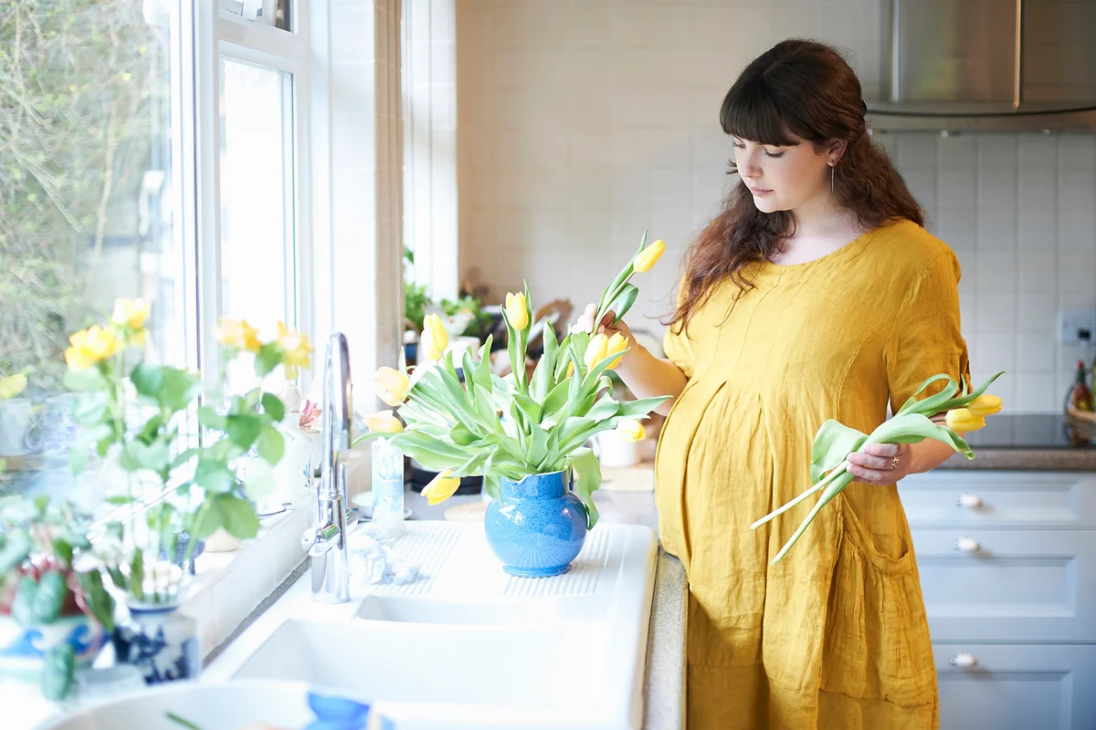 Prenant woman putting spring flowers in vase at home