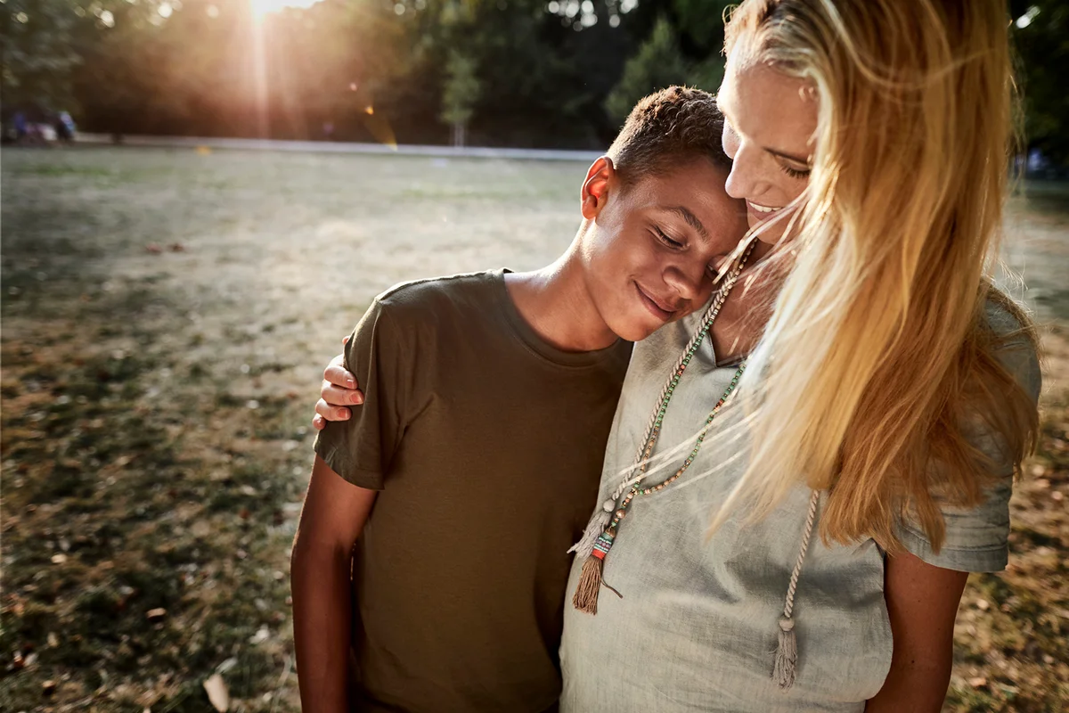 Boy leaning against pregnant mother's shoulder in a park