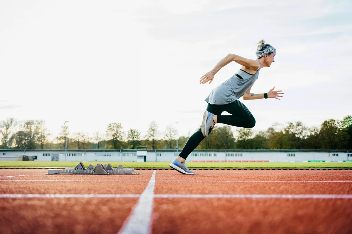 Woman Sprinting Off Starting Blocks On Outdoor Running Track