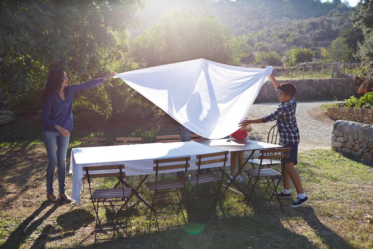 mother and son putting out white tablecloths in outdoor setting