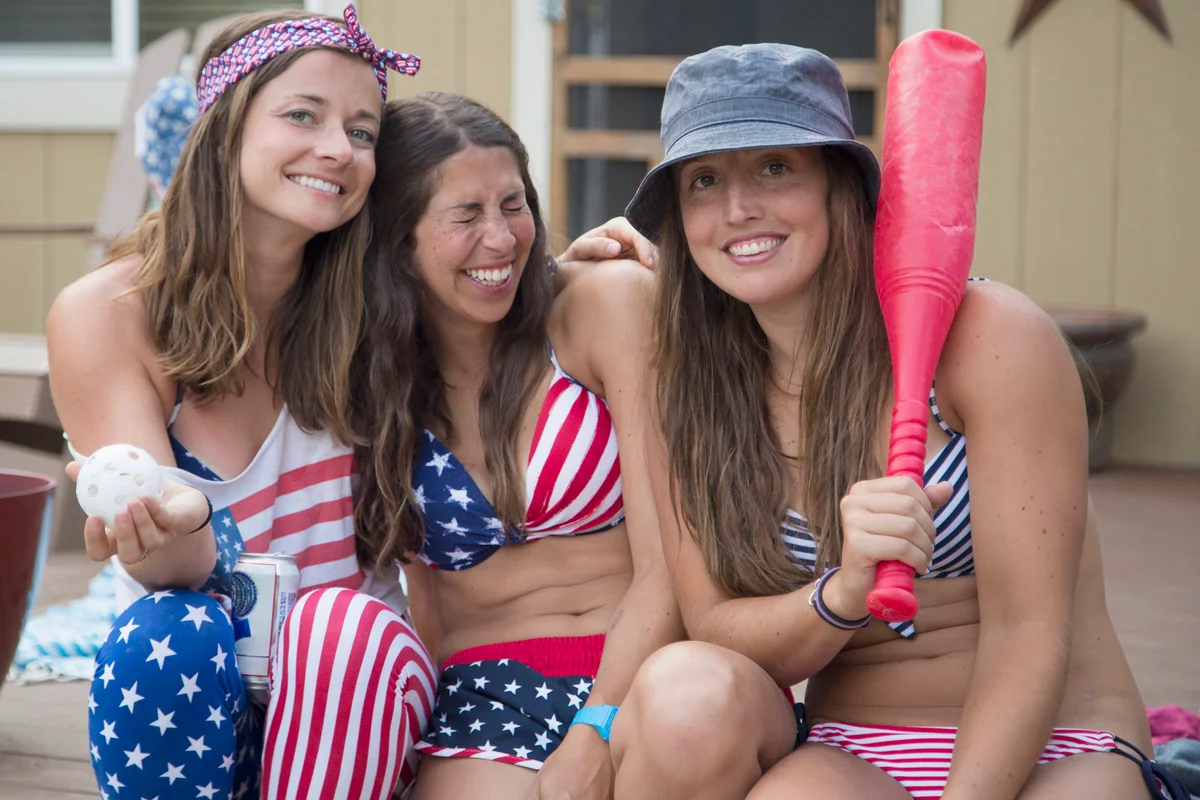 Women dressed in American flag clothing holding baseball bat and ball