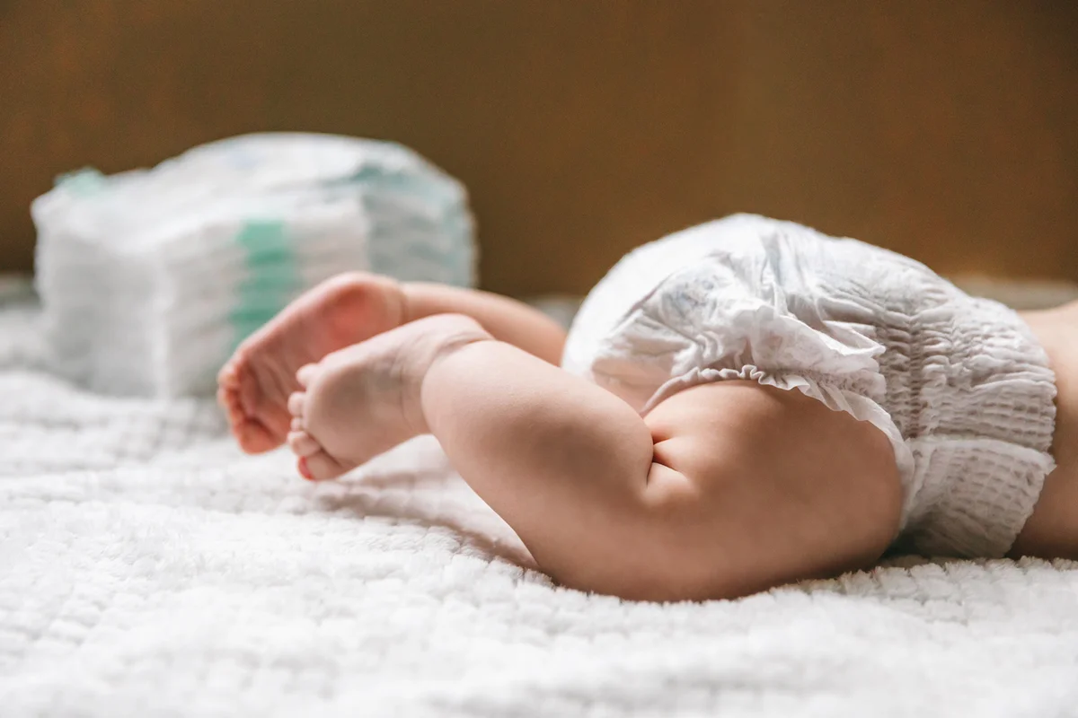 A baby in a diaper at the age of two months and a stack of diapers