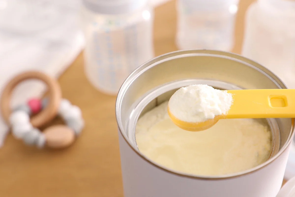 Can of powdered infant formula with scoop on table