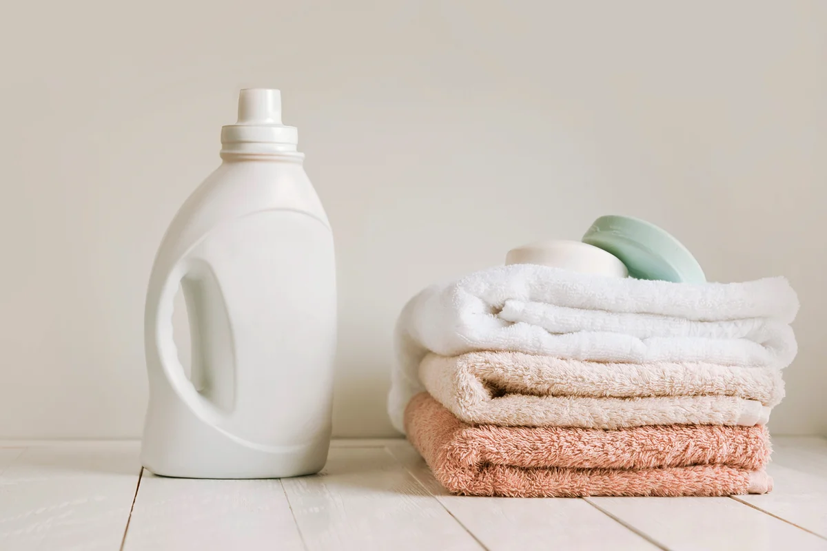 A stack of clean towels after washing and a white bottle with gel for linen