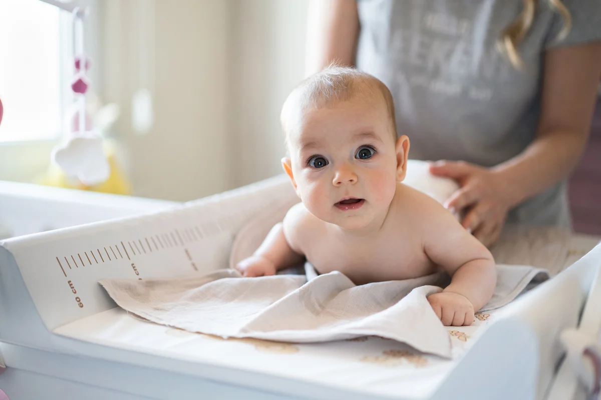 Cute baby girl in diaper on changing table at home