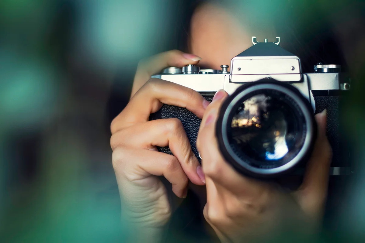 Woman photographer shooting with an analog camera between tree leaves at sunset