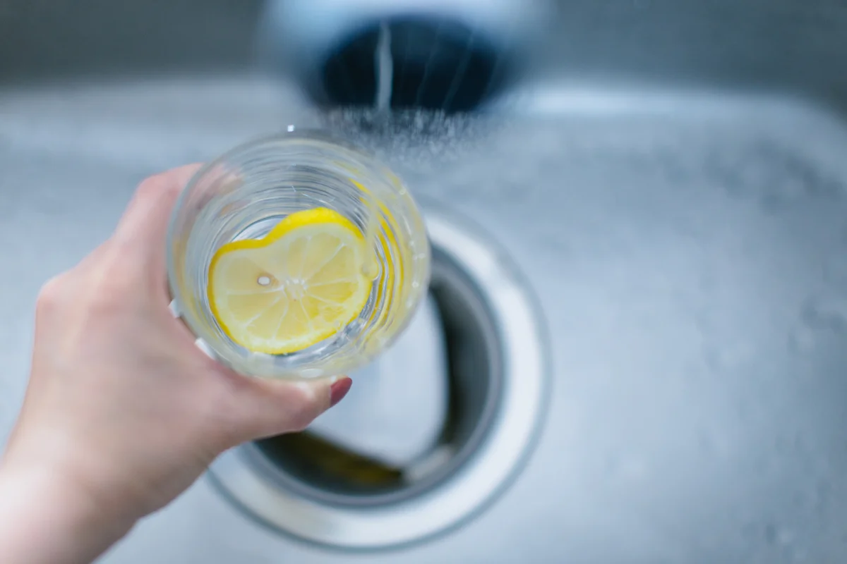 Cup of water with lemon over garbage disposal in sink
