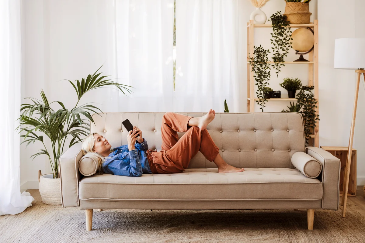 Young woman using mobile phone lying on sofa at home