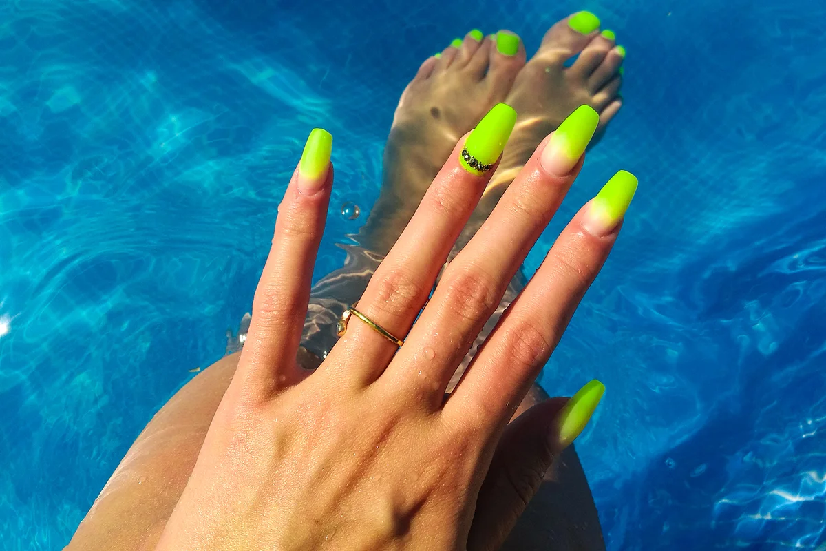 Woman Fingers With Nail Art Manicure with Neon Green Colour in a Swimming Pool