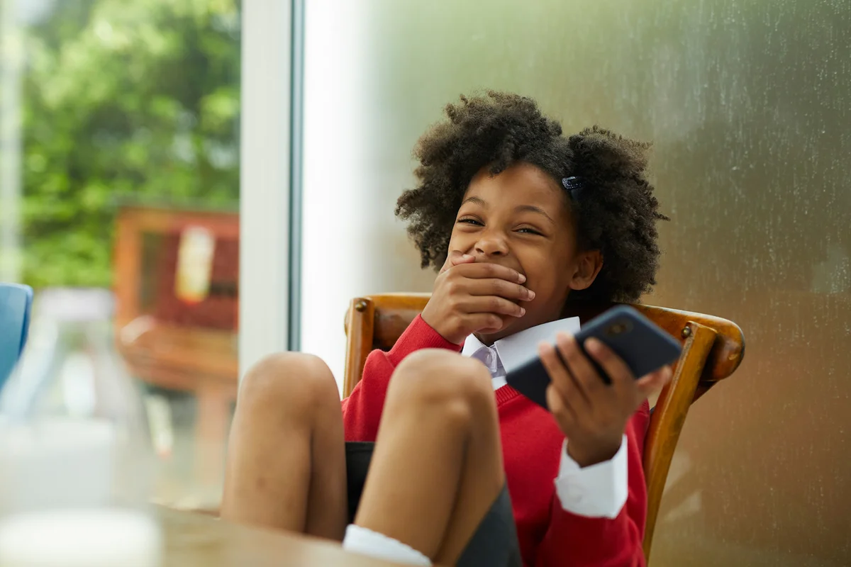 A girl wearing school uniform at breakfast at home laughing and playing on a smartphone