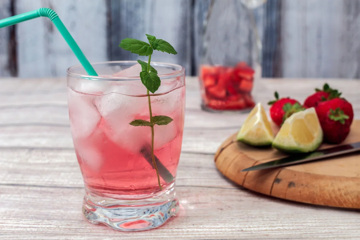 A glass of pink lemonade with ice and a sprig of mint