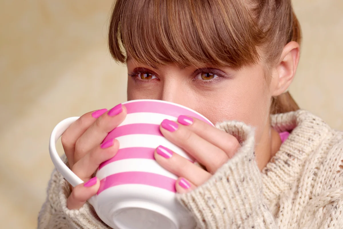 Woman with pink nails drinking from a cup