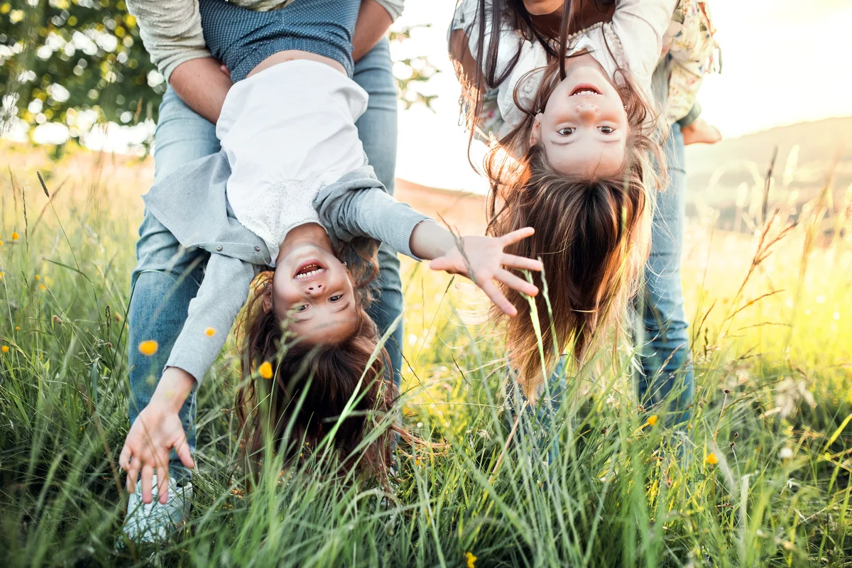 Parents holding their daughters upside down in a field