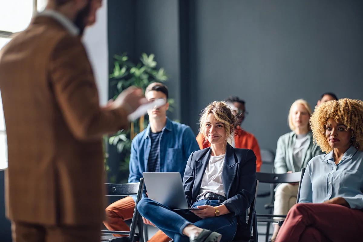 Group of men and women sitting and listening to a seminar. They are smiling.