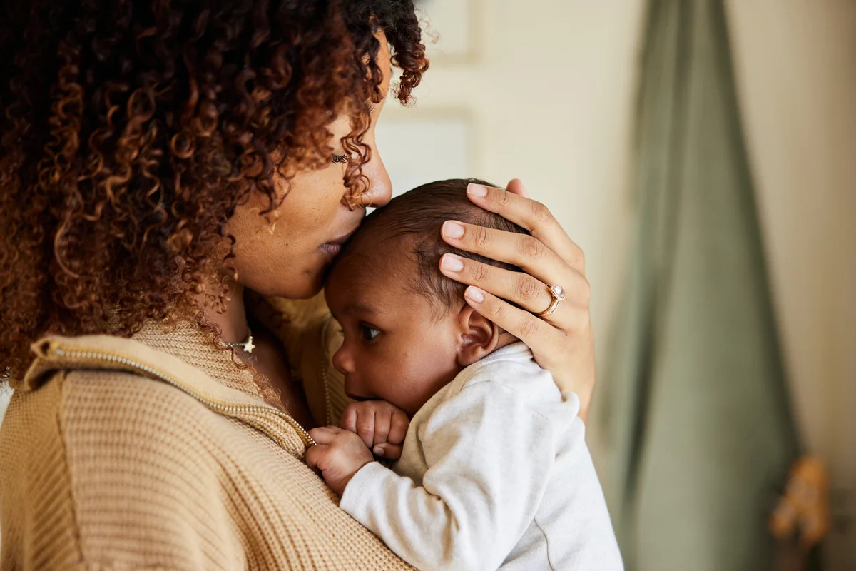 Mother kissing her adorable little baby boy cradled in her arms at home