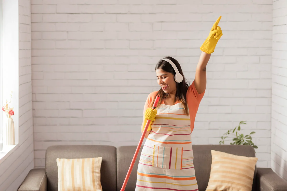 Cheerful woman dancing while sweeping floor with broom