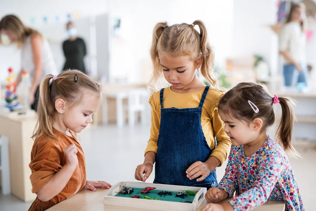 pre-school girls friends playing with artificail insects indoors in nursery