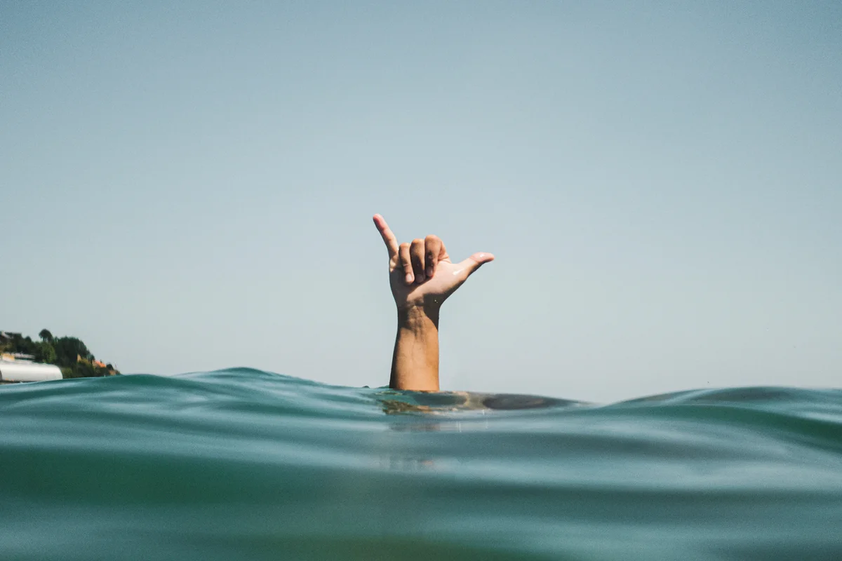 Womans hand making surfer's sign in water -