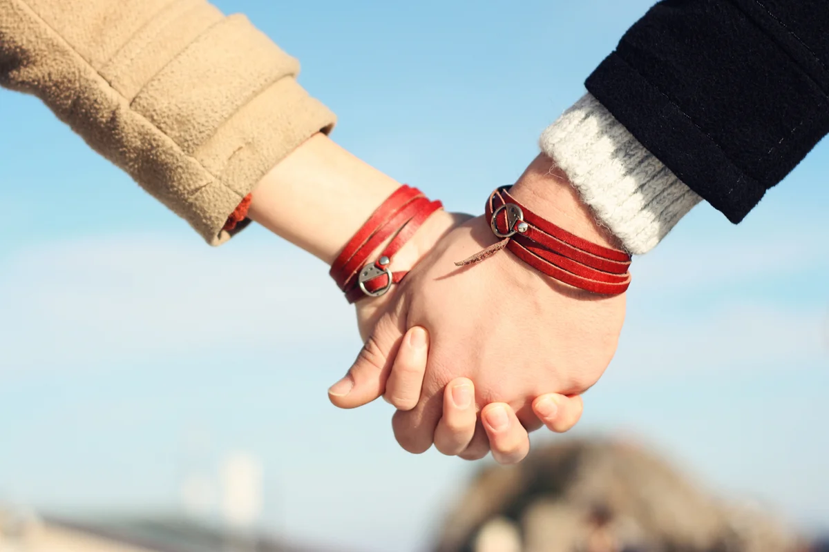 Two people holding hands with identical red leather friendship bracelets
