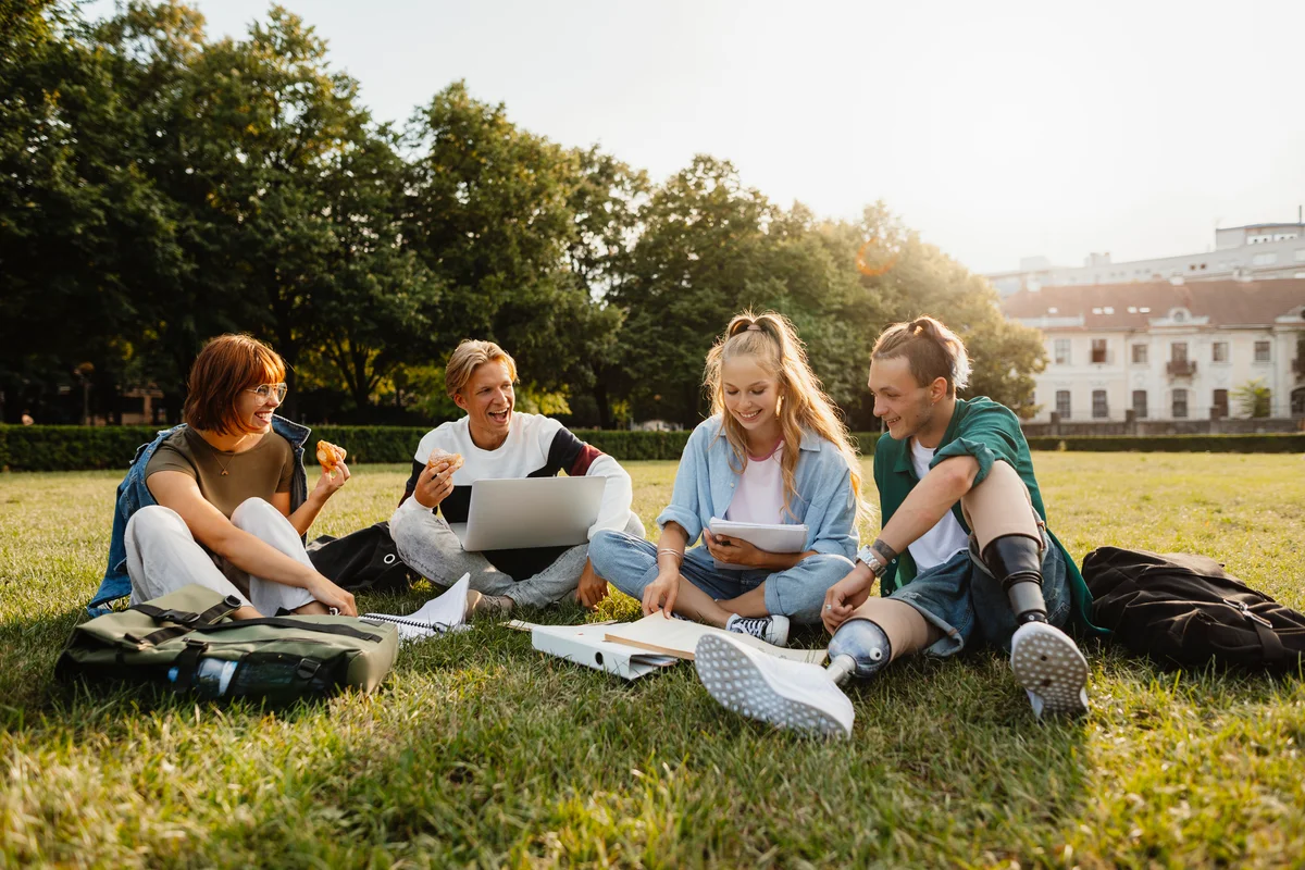 Students using laptop and sitting on grass outdoors in campus area