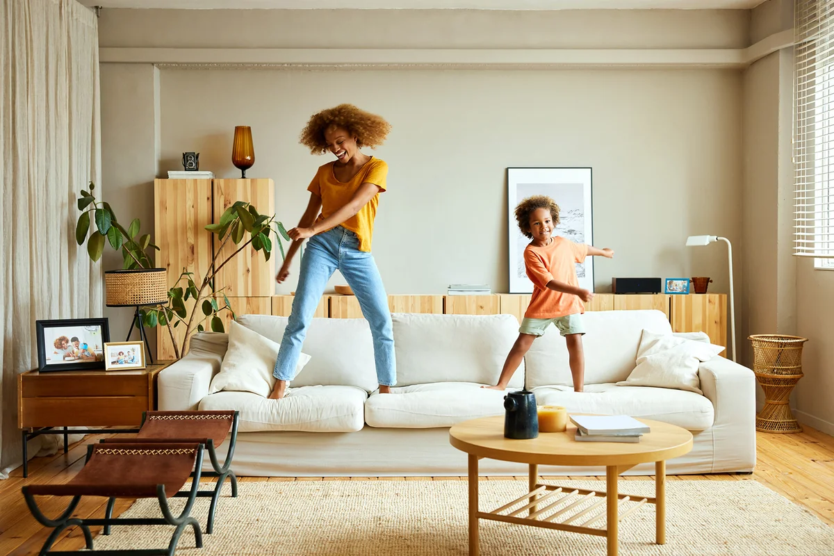 Happy mother and son dancing on sofa at home