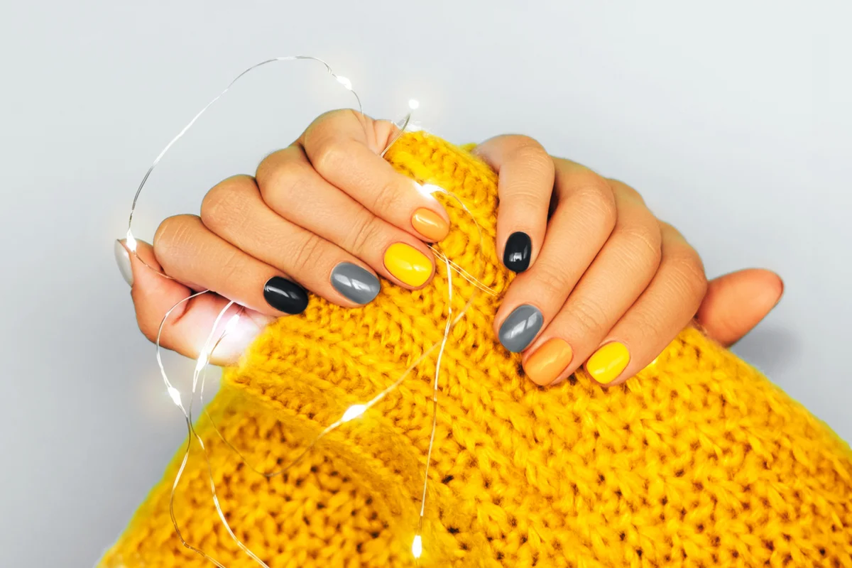 Multicolored manicure with yellow and gray nails on light background
