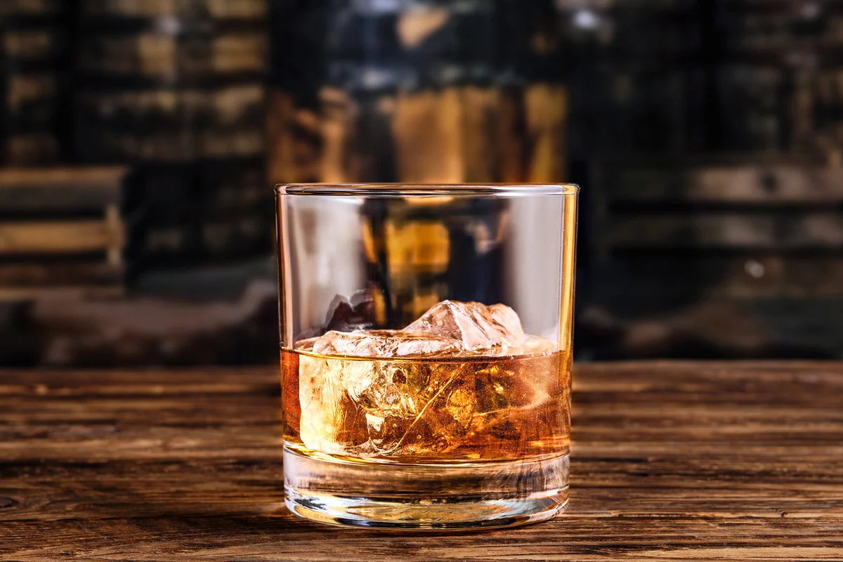 Glass of whiskey with ice with barrels