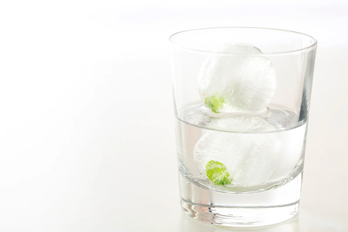 Ice balls with mint leaves in a glass of water