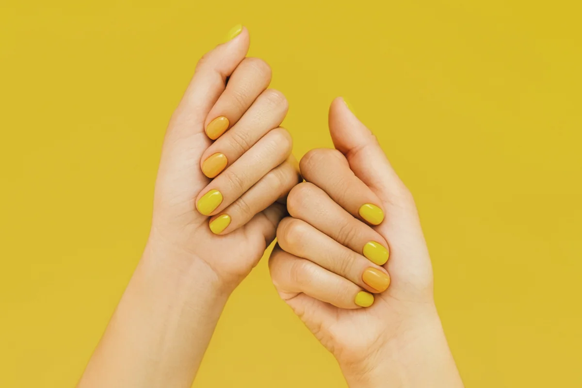Female hands with bright yellow and orange colorful manicure against yellow background