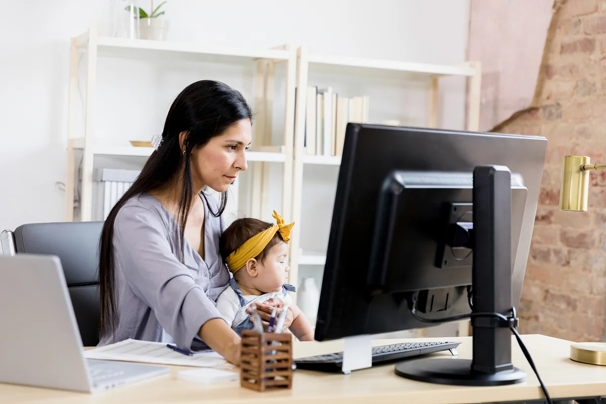 Serious, focused mother holds baby while working from home