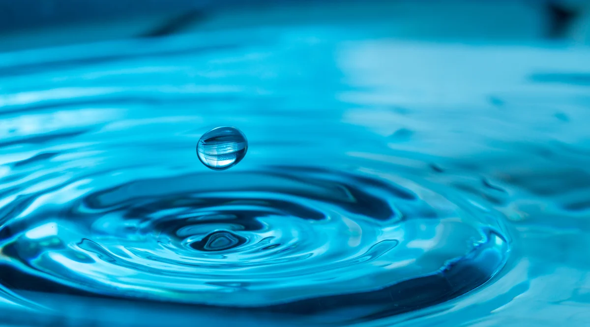 Calming picture of water droplet creating ripple in blue water