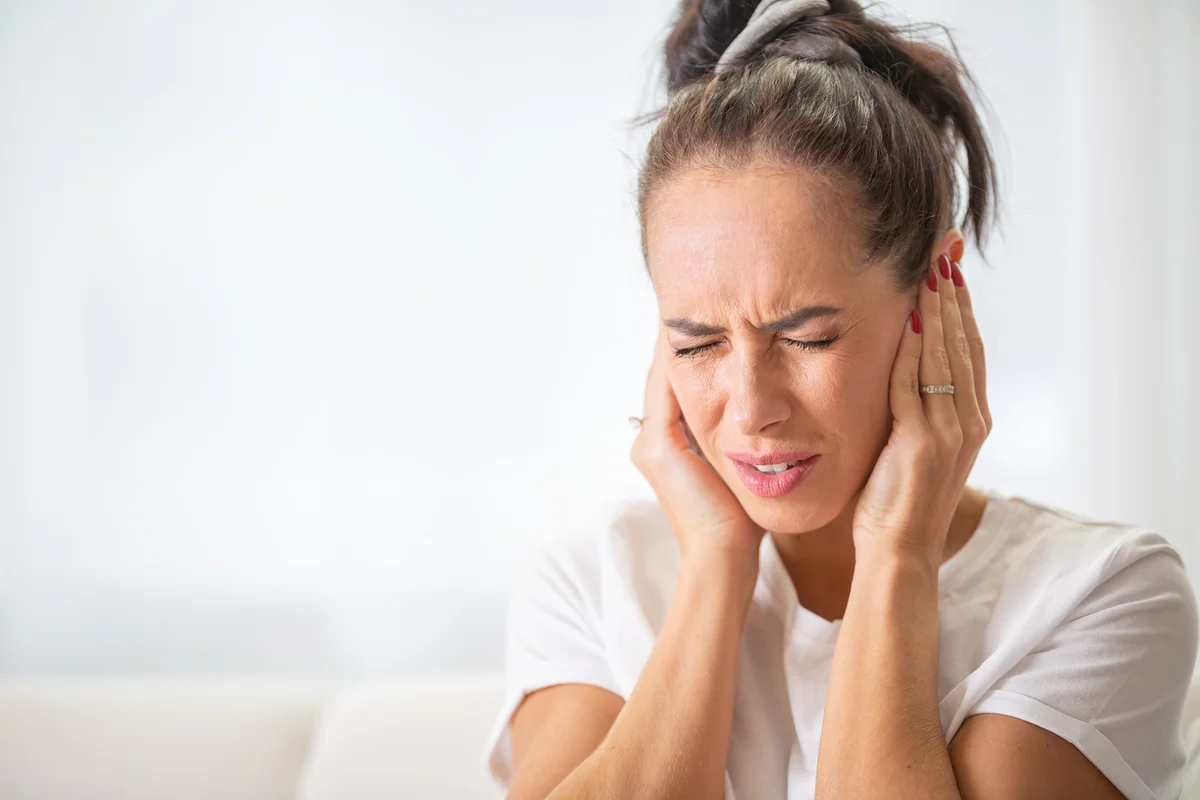 Woman closes hear ears with hands due to noise