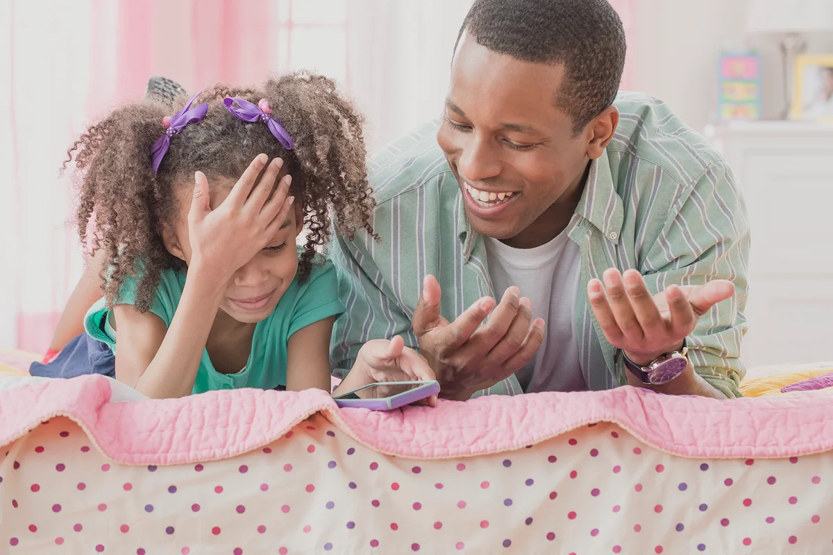 Father and daughter using cell phone together on bed