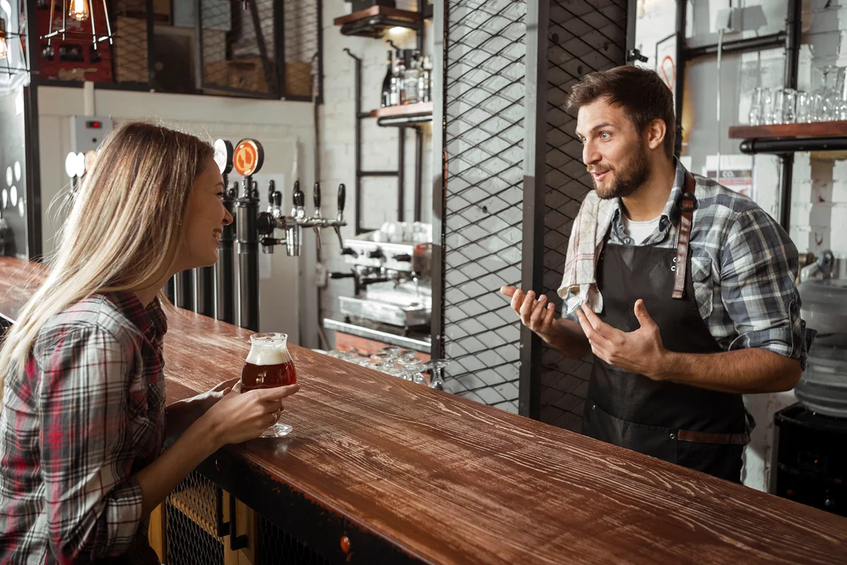 Young bartender talking to a female customer in pub
