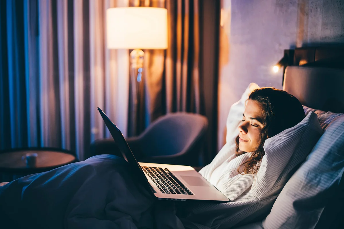 Young woman laying in bed and using laptop at the night.