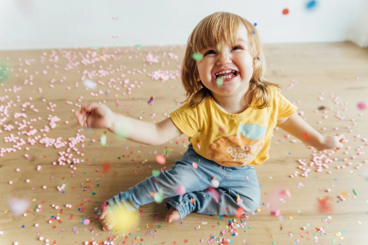 A girl smiling as a shower of colored confetti falls on her