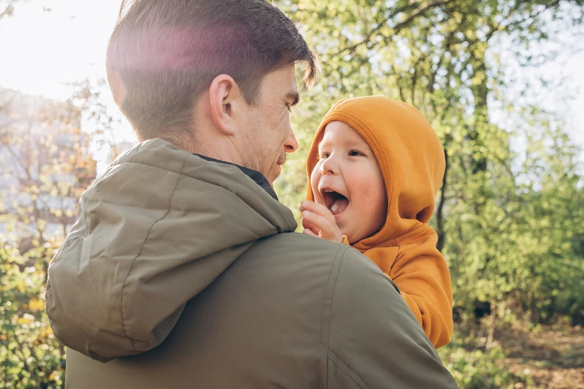 Happy cute baby boy with father standing in front of trees