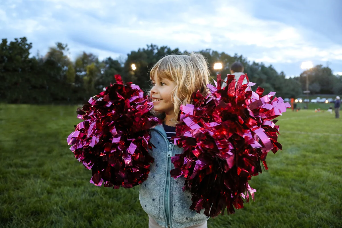 Little girl holding pompoms at sports event at dusk