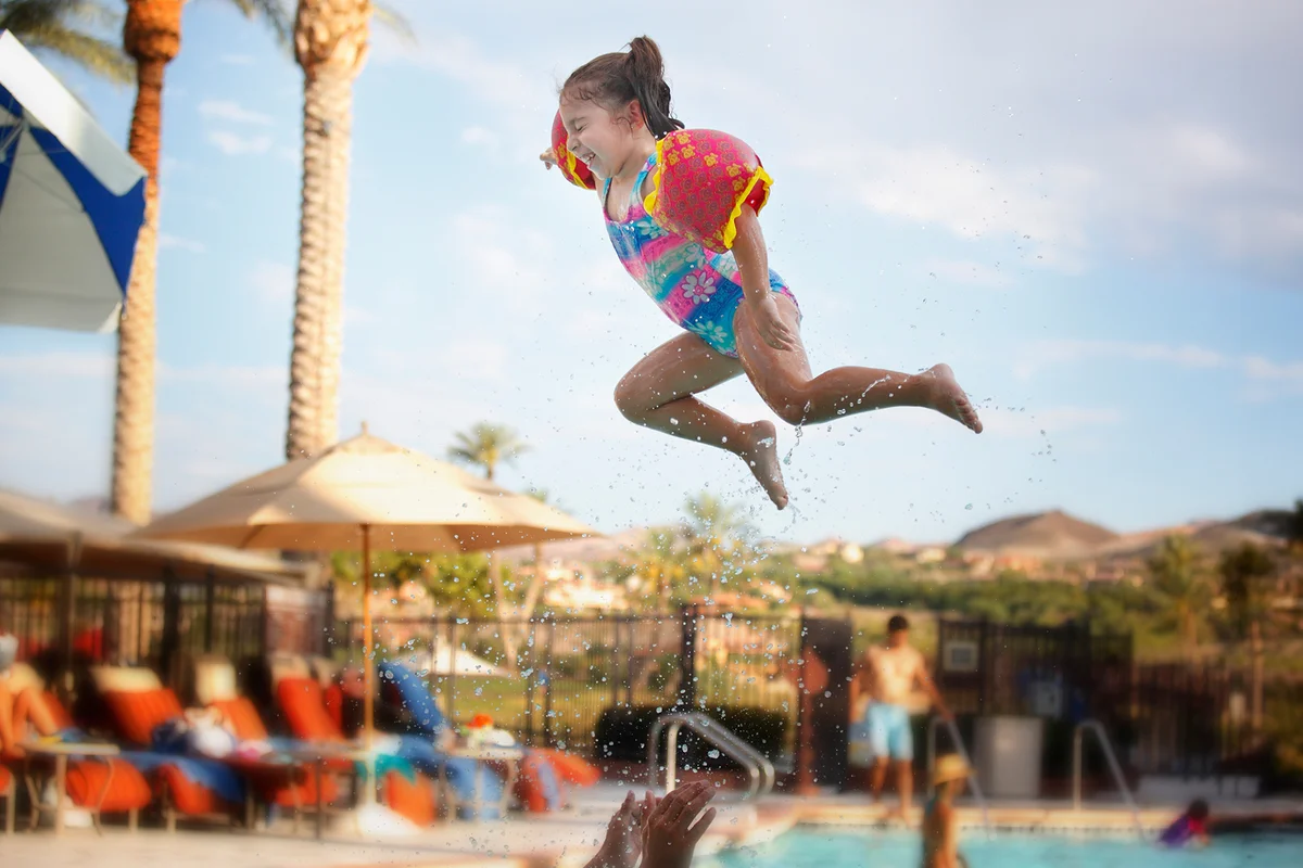 Girl laughs as she flies through air above swimming pool in desert.