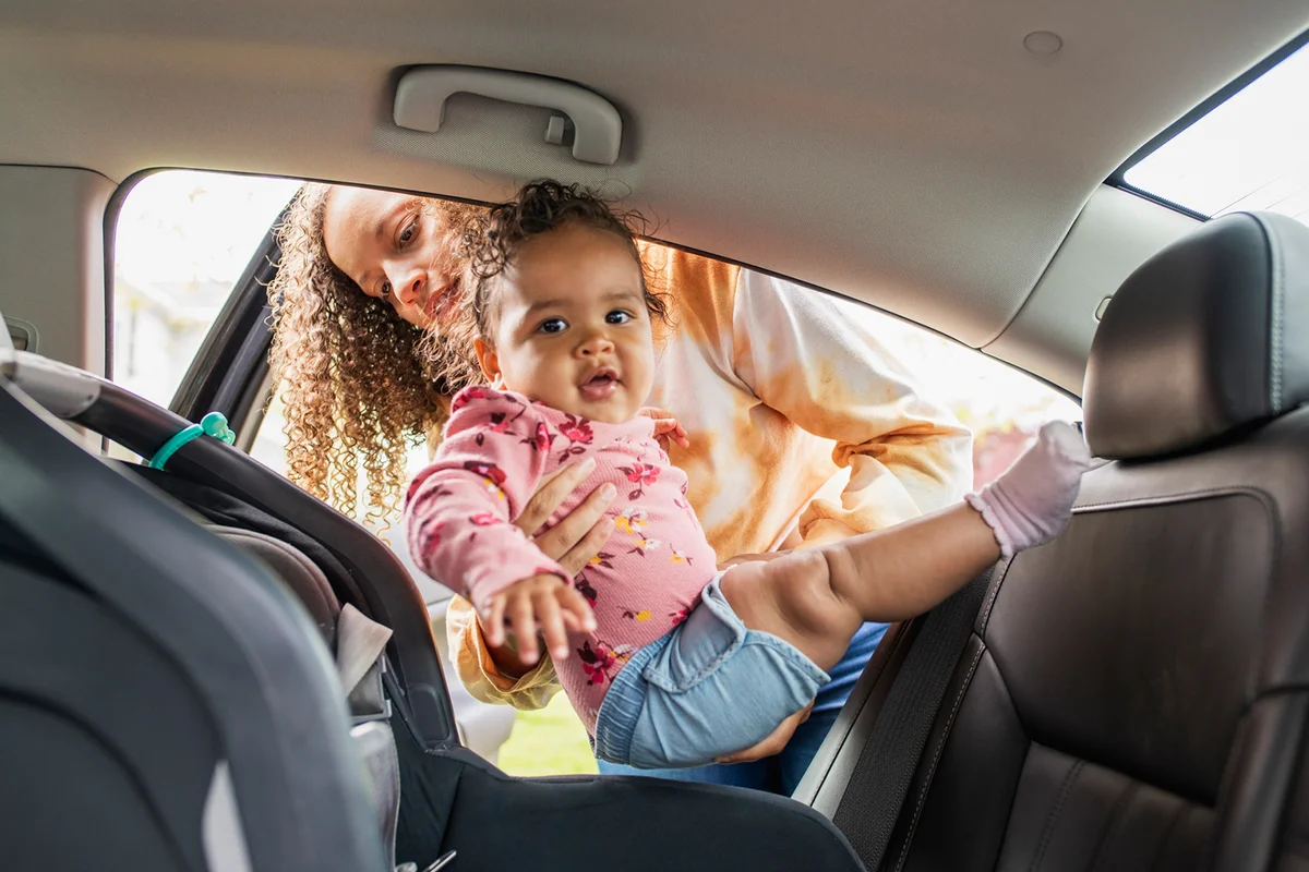 Young mother placing infant daughter in car seat