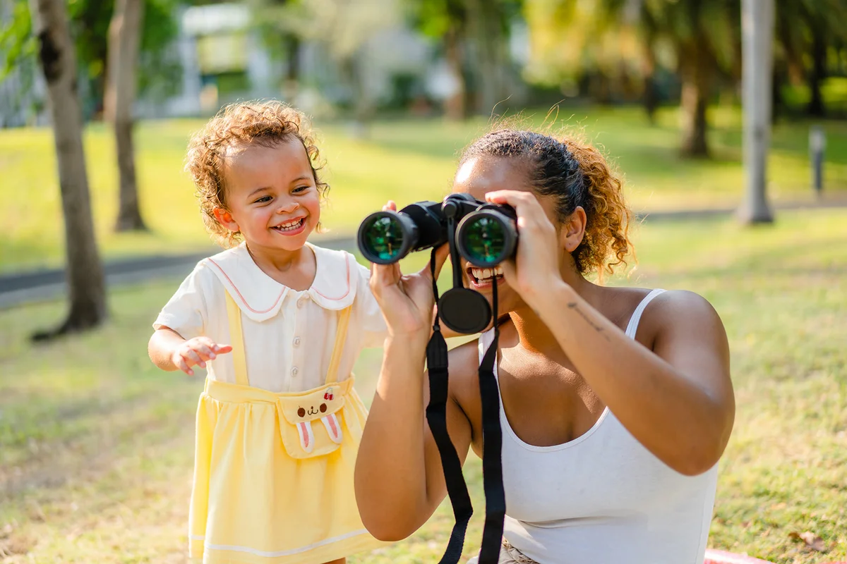 A young mother and a child playing with a binocular while picnicking in a park
