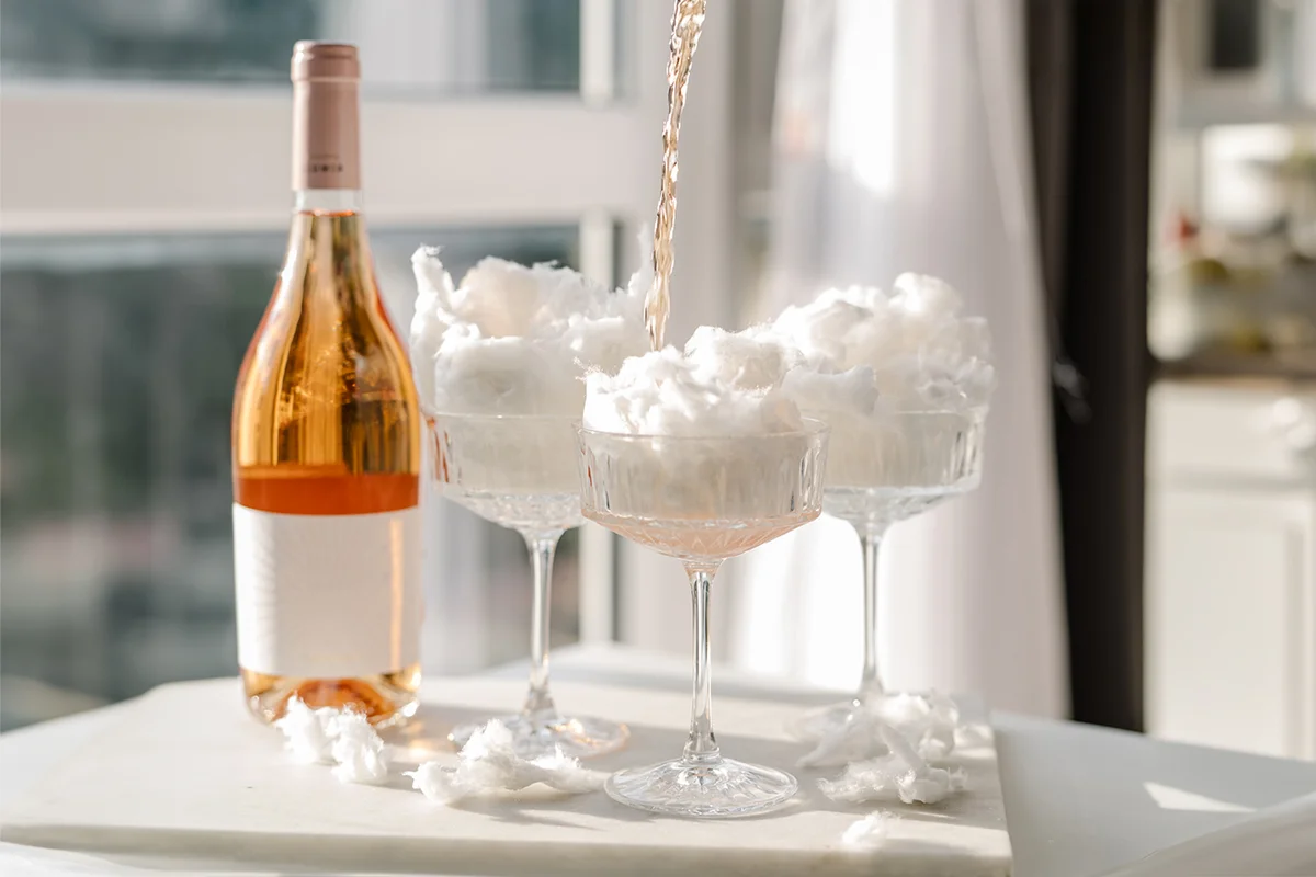 A bottle of sparkling wine rose pouring liquid with glasses and cotton candy